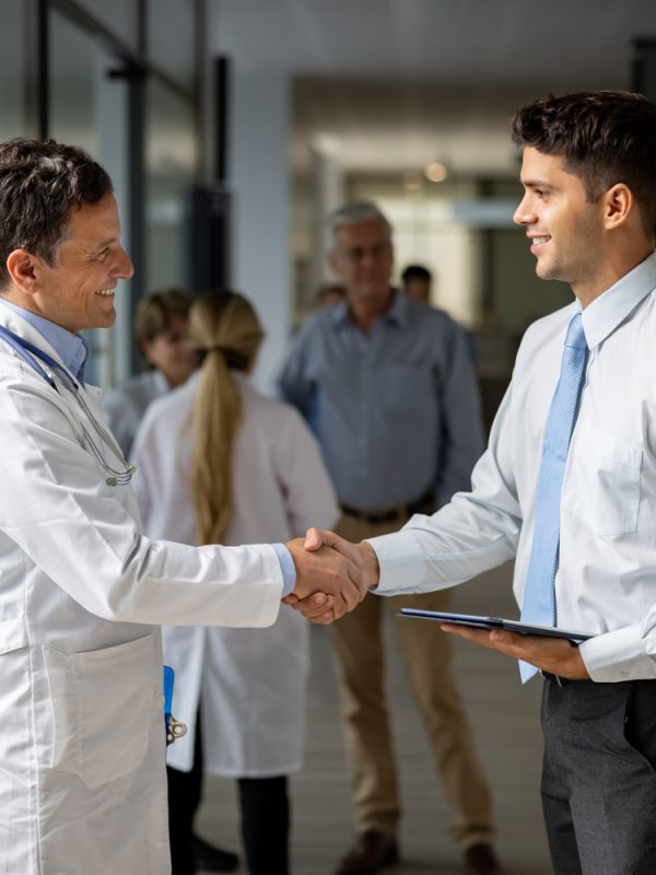 Latin American medical sales representative greeting a doctor with a handshake at the hospital while presenting some medicines - pharmaceutical industry concepts